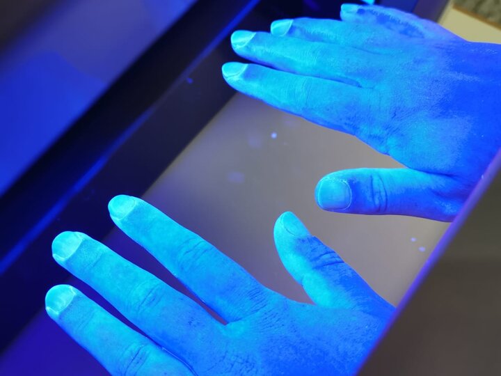 Hände werden in eine Schwarzlichtlampe gehalten