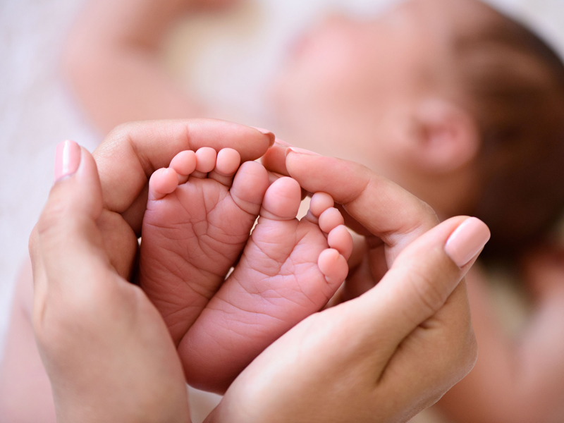 Hand hält Babyfuesse - herzfoermig
