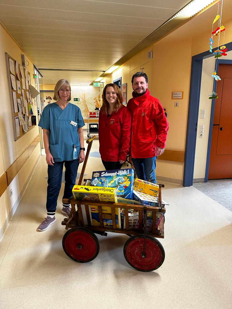 Personen lachen in die Kamera. Vor ihnen steht ein Wagen mit Spielsachen