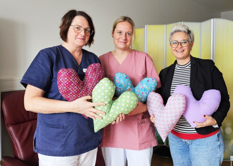Drei Frauen halten große bunte Herzkissen für Brustkebspatientinnen in den Händen