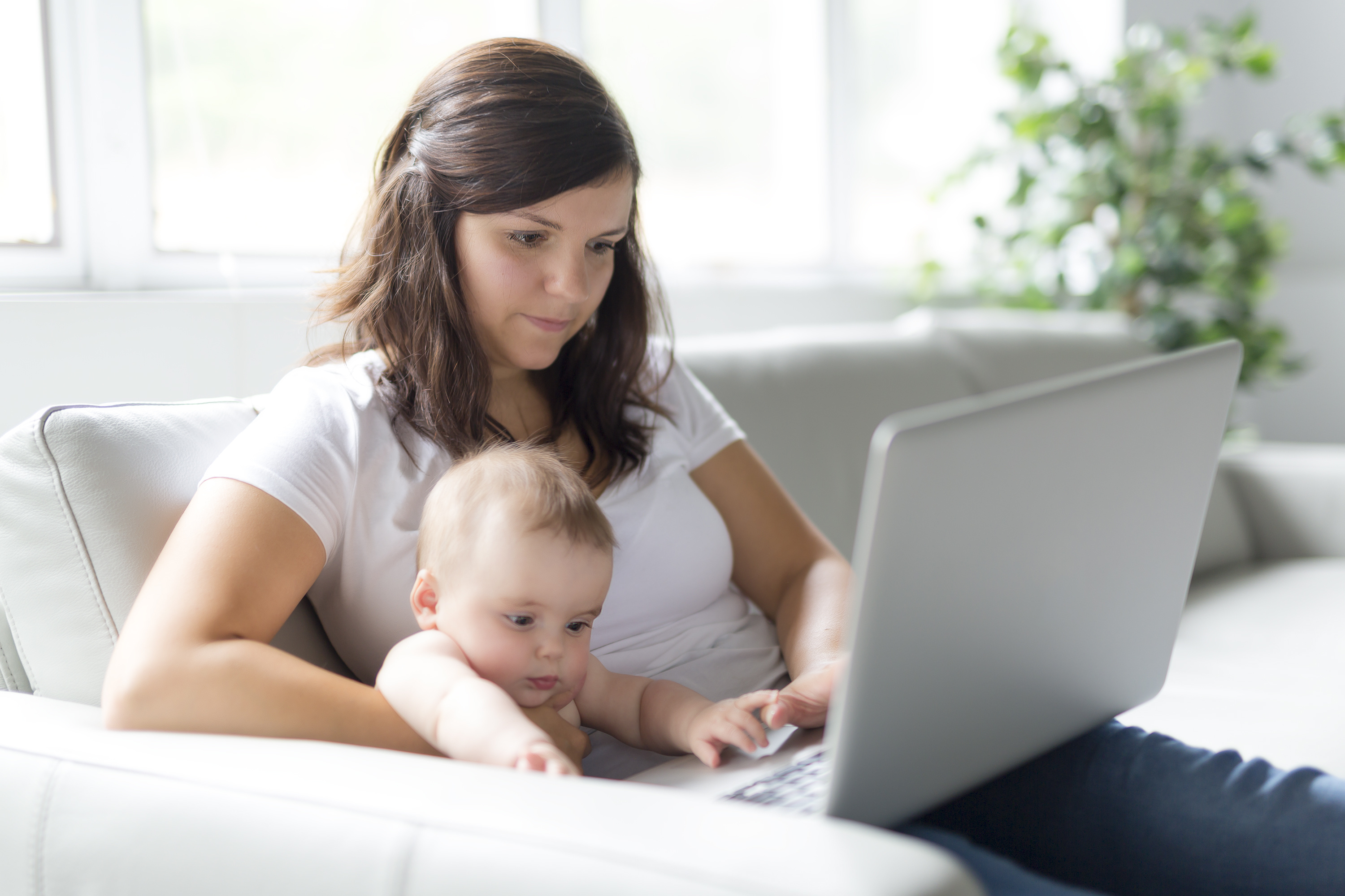 Junge Mutter mit Baby sitzt auf der Couch und chattet mit TeleHebamme